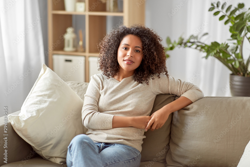 people, race, ethnicity and portrait concept - happy african american young woman sitting on sofa at home people, race, ethnicity and portrait concept - happy african american young woman sitting on sofa at home