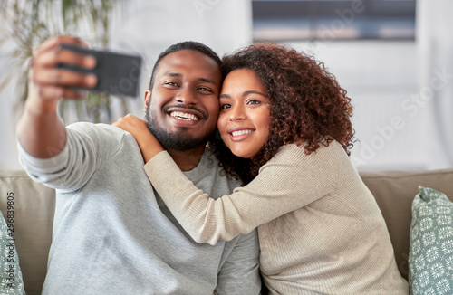 family, technology and people concept - happy african american couple with smartphone taking selfie at home