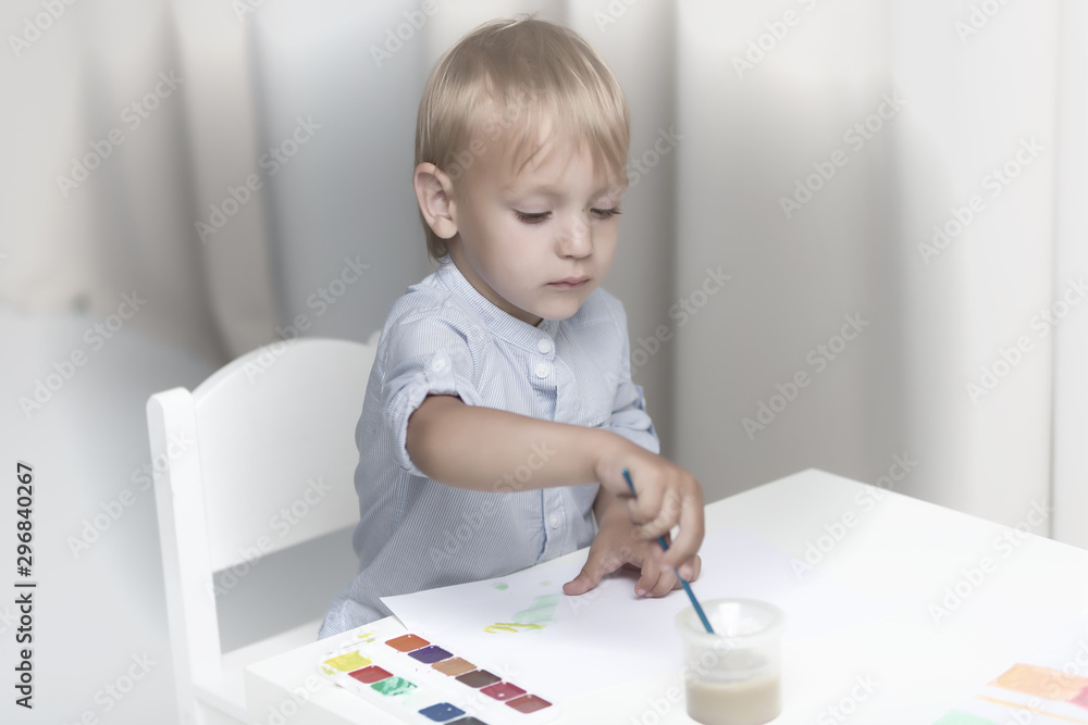Cute little boy paints with watercolors while sitting at the tab Cute little boy paints with watercolors while sitting at the tab