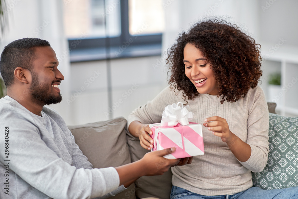 holiday, greeting and people concept - happy african american couple with gift at home holiday, greeting and people concept - happy african american couple with gift at home