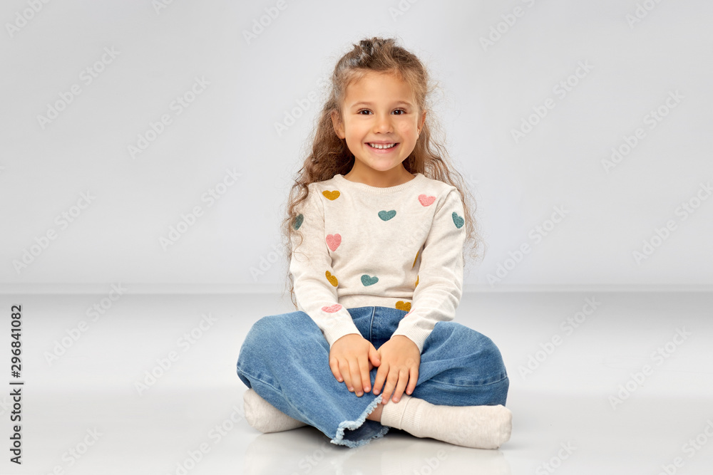 childhood and people concept - beautiful smiling girl sitting on floor over grey background childhood and people concept - beautiful smiling girl sitting on floor over grey background