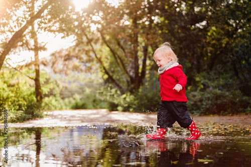 niedliches kleinkind mit roter Jacke spielt in einer Regenpfütze, Spiegelung Sonnenschein