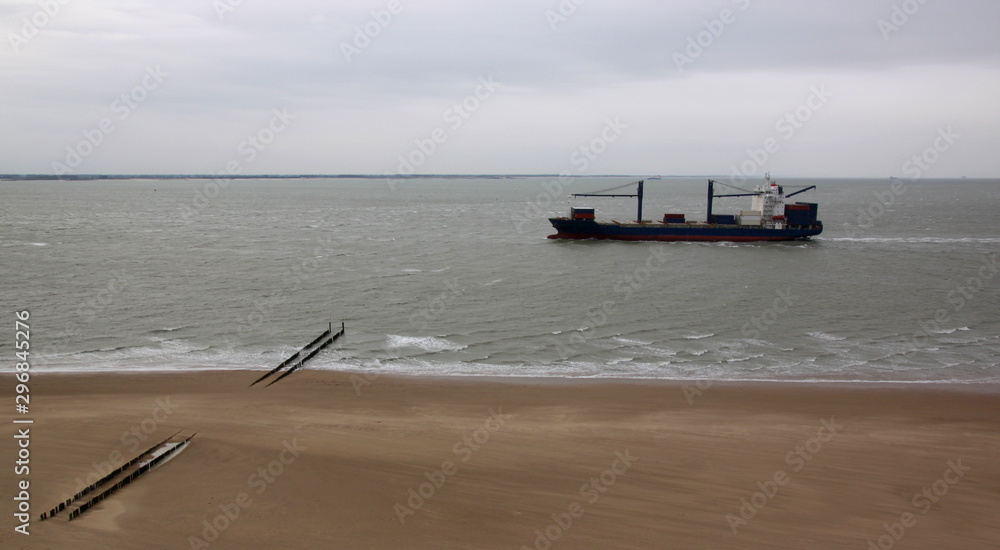 Obraz premium Panoramic view of an empty container ship passing a North Sea beach on a cloudy day in Vlissingen, Netherlands