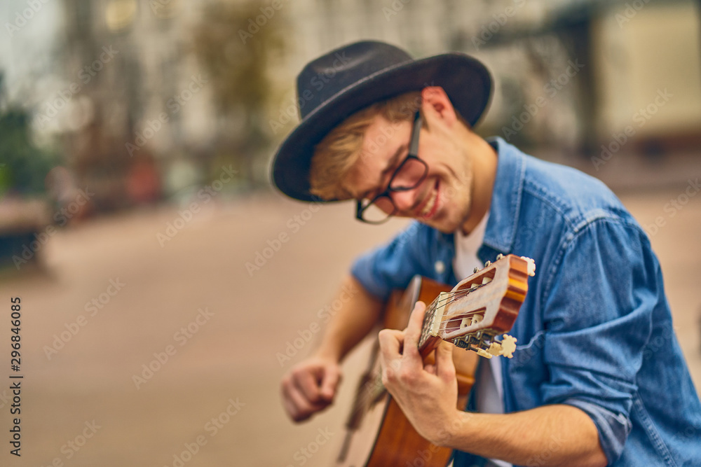 Young man playing the guitar. Stylish hipster guy with hat enjoys music and holidays.