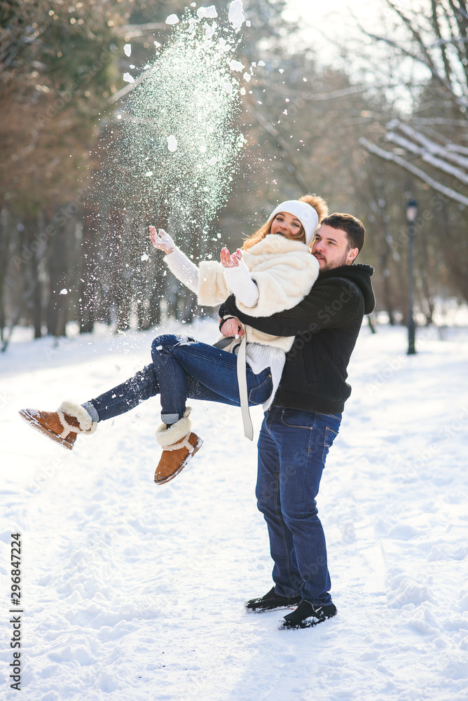 Beautiful girl throws snow while her courageous handsome boyfriend holds her in the hands.