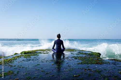 Yoga woman meditation at the seaside cliff edge facing the coming strong sea waves