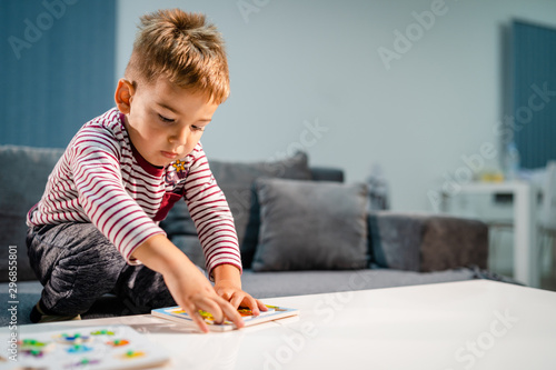 Small boy little playing at home alone by the table with puzzle developing mental skill having fun learning
