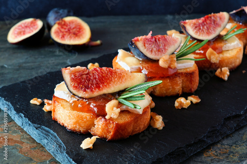 Crostini appetizers with figs, brie cheese and walnuts. Close up on a slate serving board against a dark background.
