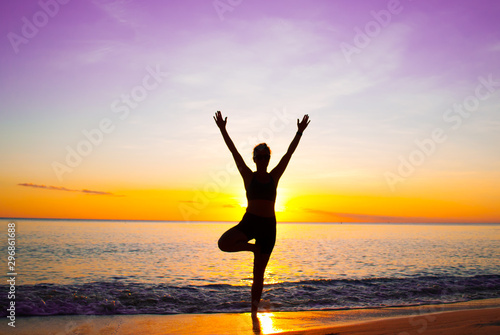 A young lady practices yoga on the beach in front of the setting sun. The Caribbean sea is tranquil as it laps the sandy coastline of the idyllic island © drew