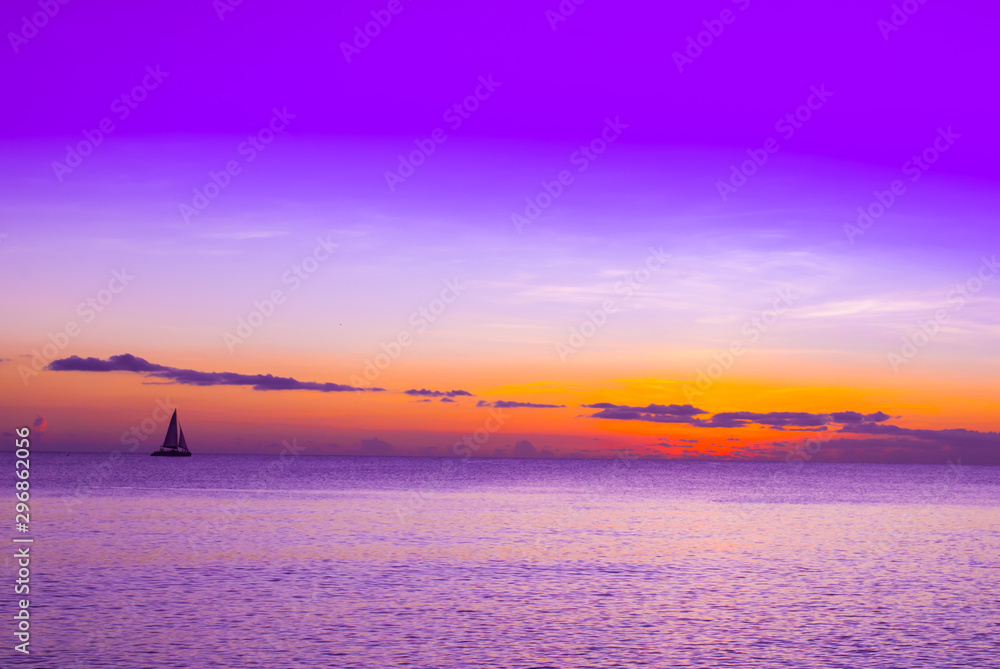 A sailboat shot against the setting sun in the tropical waters of the Cayman Islands.
