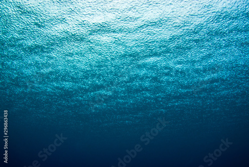 A shot taken from beneath the surface of the sea looking up at the sky. The light patch is the sun overhead and through the surface it is possible to see the rain falling hard on the water