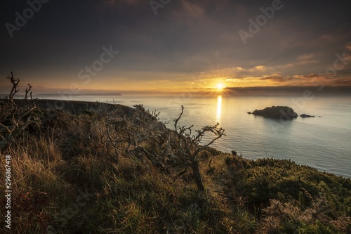 Breathtaking sunset over the sea with a small hill in the corner in Nare Head, Cornwall, UK photo