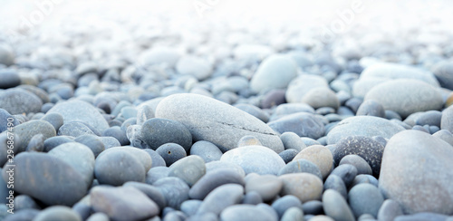 Round stones on a dry river bed outside in nature. Smooth pebbles with light gray tones in ambient light.