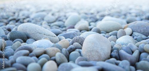 Round stones on a dry river bed outside in nature. Smooth pebbles with light gray tones in ambient light.