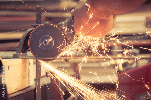 Person inside a metal smith blue collar labor workshop carefully using a metal angle grinder power tool and getting hit by hot flying dangerous sparks on his bare unprotected hand