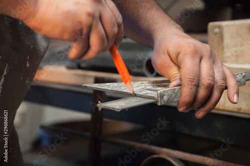  On workshop interior work bench table counter top a man makes a quick marking swipe with a pencil to mark his next cut upon a piece of steel