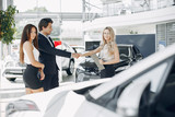 People in a car salon. Man buying the car. Elegant women with handsome man