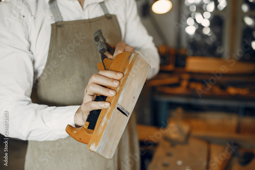 Man working with a wood. Carpenter in a white shirt. Man with a chisel