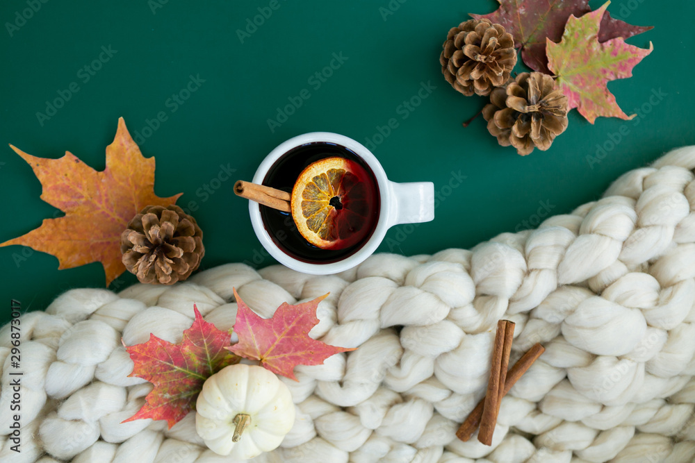 Spiced cider with orange and cinnamon on green background with fall leaves and pinecones, chunky wool knit blanket - obrazy, fototapety, plakaty 