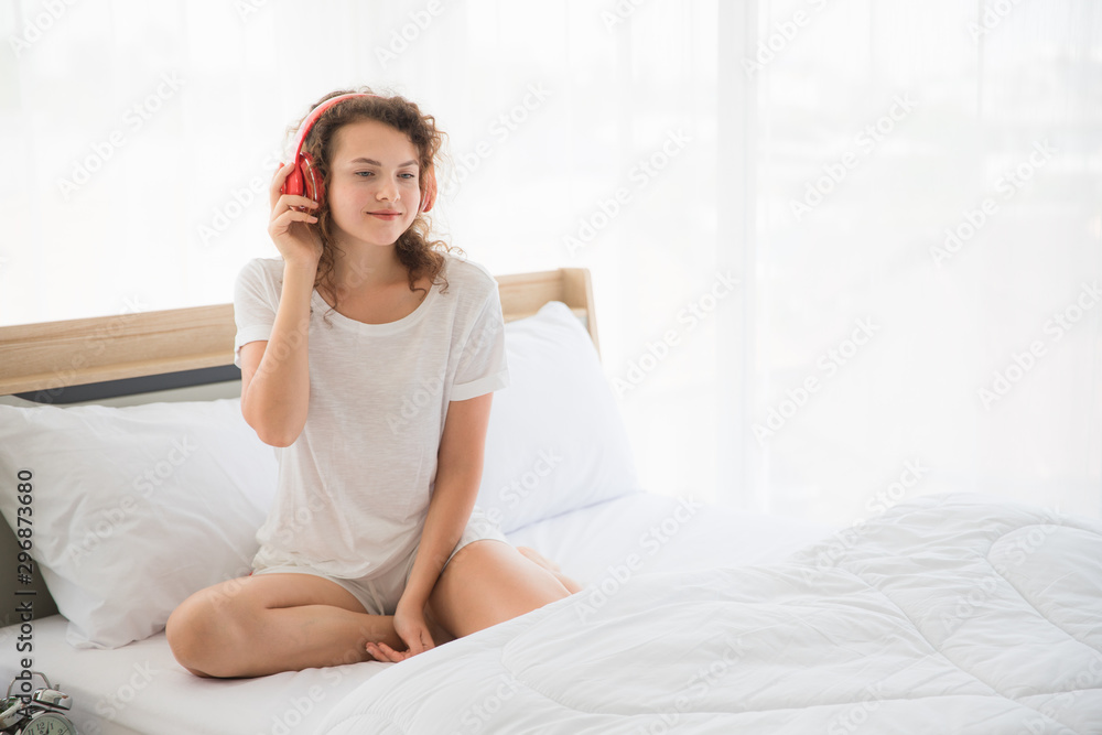 Beautiful women wear white shirts. She wears headphones and listens to music and smiles happily in her bedroom in Bangkok, Thailand in the morning. Concept for a comfortable holiday Beautiful women wear white shirts. She wears headphones and listens to music and smiles happily in her bedroom in Bangkok, Thailand in the morning. Concept for a comfortable holiday