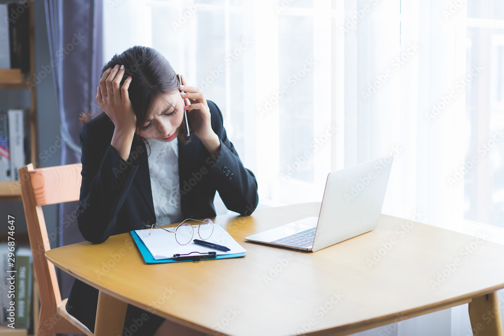 Asian women are talking on the phone and sitting on the desk with laptop, documents and glasses placed. She tilted her neck, using her grip on her head And has a face that looks stressful. Asian women are talking on the phone and sitting on the desk with laptop, documents and glasses placed. She tilted her neck, using her grip on her head And has a face that looks stressful.