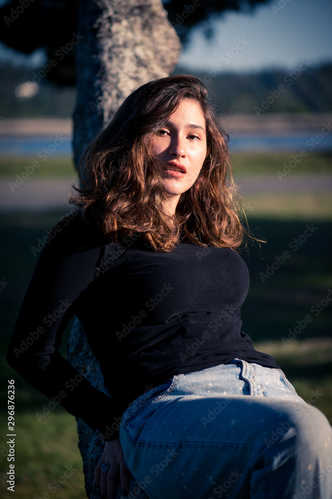 Beautiful young woman mixed ethnicity 20s sits on tree branch