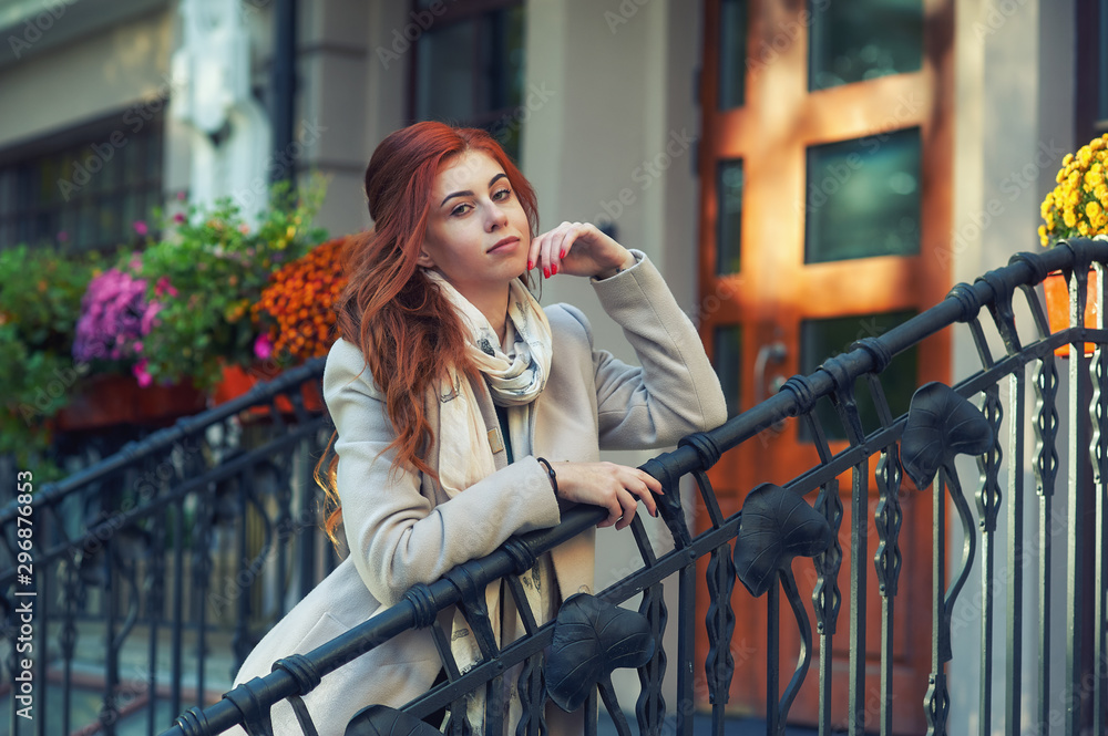 Obraz premium Portrait of a young woman in the autumn city . A girl with red hair in a beige coat
