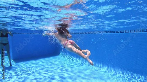 underwater view of six years old child, with diving mask, diving towards her mother arms in clear water of pool. Funny and tender scene