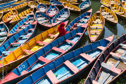 colorful boats in Fewa lake in Pokhara, Nepal with women in red sitting inside © anyabr