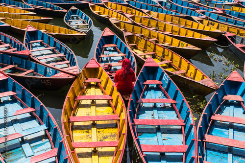 colorful boats in Fewa lake in Pokhara, Nepal with women in red sitting inside © anyabr