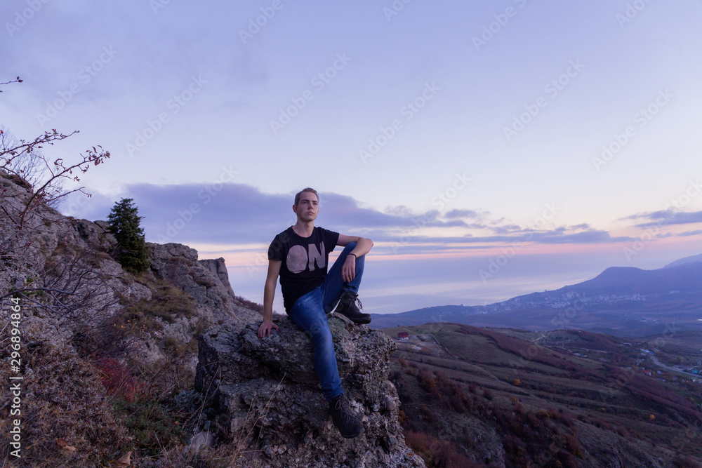 Young attractive man located with on the top of mountains against the backdrop of a purple sunset, Young attractive man located with on the top of mountains against the backdrop of a purple sunset,