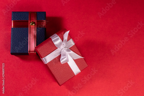 Red and blue gift boxes shot from top, decorated with ribbons on red background with copy space