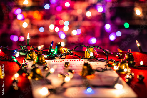 Jingle Bells Sheet Music lit by Christmas lights, surrounded by various bells. Shallow depth of field with heavy bokeh.
