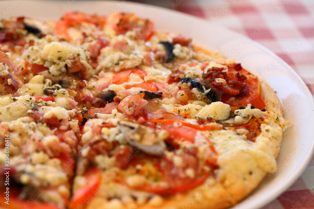 Pizza with mushrooms, tomatoes, spices on a white plate and a checkered tablecloth. Pizza with mushrooms, tomatoes, spices on a white plate and a checkered tablecloth.