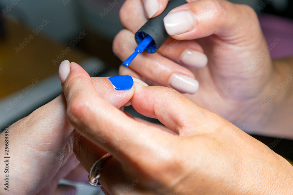 Beautiful manicure process. Nail polish being applied to hand, polish is a blue color. close up Beautiful manicure process. Nail polish being applied to hand, polish is a blue color. close up