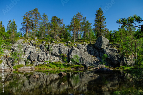 Trees and stones reflection on little lake on mountain Vottovaara, Karelia, Russia