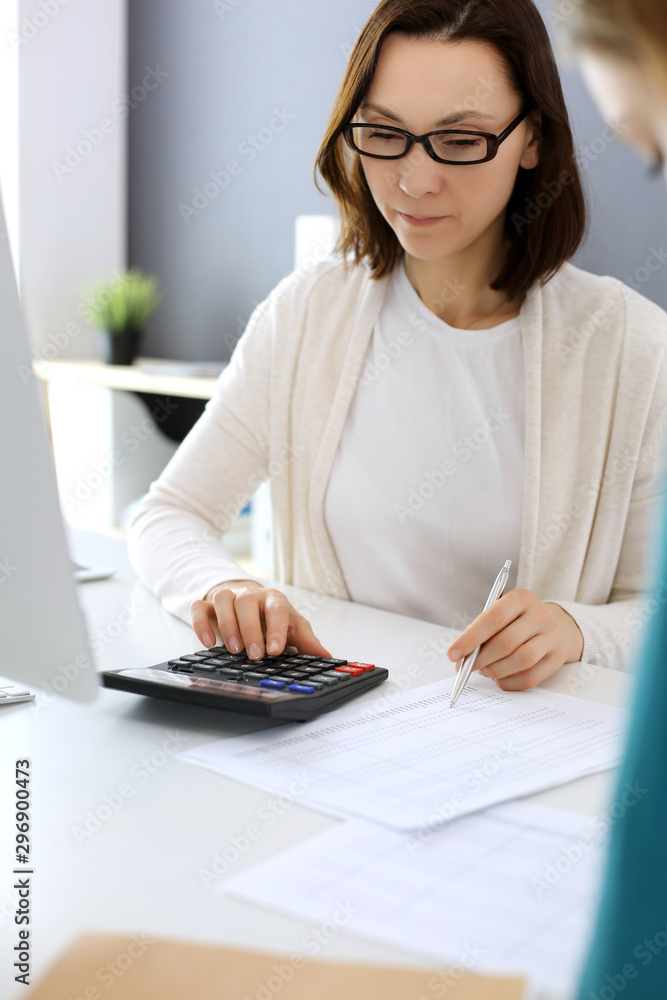 Accountant checking financial statement or counting by calculator income for tax form, hands close-up. Business woman sitting and working with colleague at the desk in office. Audit concept Accountant checking financial statement or counting by calculator income for tax form, hands close-up. Business woman sitting and working with colleague at the desk in office. Audit concept