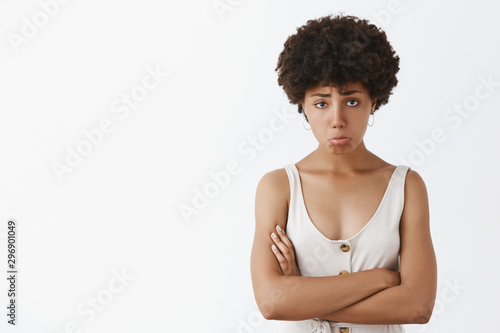 Girl feeling upset and disappointed after losing cometition, standing silly and gloomy with sad expression over gray background, holding hands crossed, pouting and frowning, whining and complaining photo