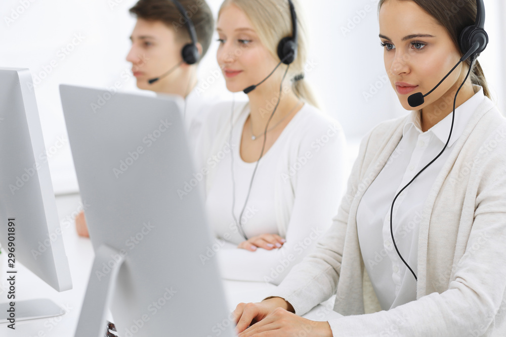 Call center. Group of operators at work. Focus on beautiful woman receptionist in headset at customer service white colored office. Business concept Call center. Group of operators at work. Focus on beautiful woman receptionist in headset at customer service white colored office. Business concept