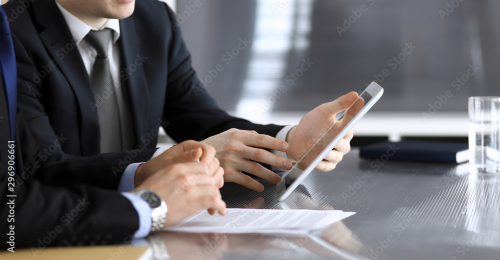 Businessman using tablet computer and work together with his colleague or partner at the glass desk in modern office, close-up. Unknown business people at meeting. Teamwork and partnership concept - obrazy, fototapety, plakaty 