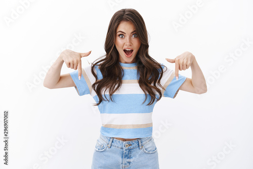 Speechless impressed gorgeous woman spot incredible offer and tell girlfriend exciting news, pointing down, indicate fingers bottom copy space, stare camera astonished and amazed white background