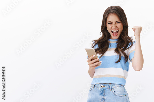 Excited joyful lucky girl extremely happy win bit boyfriend score, fist pump and smiling shouting hooray, hold smartphone read excellent news, receive text message, triumphing, achieve desired