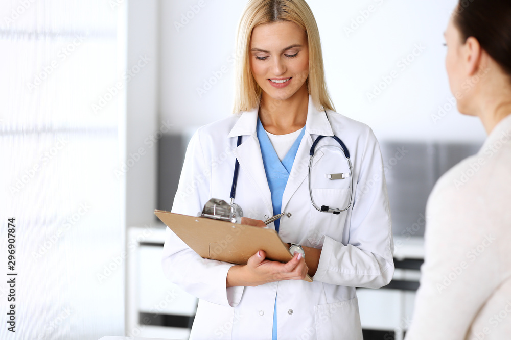 Doctor woman at work in hospital excited and happy of consulting female patient. Blonde physician controls medication history records and exam results while using clipboard. Medicine and healthcare Doctor woman at work in hospital excited and happy of consulting female patient. Blonde physician controls medication history records and exam results while using clipboard. Medicine and healthcare