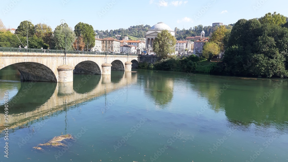Torino, Italy - 10/17/2019: Beautiful view to the river Po, with an amazing reflection of the houses and the bridge on the water. Clear blue sky and autumn coloured trees in the background. 
