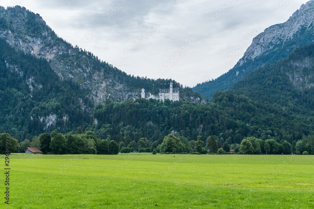 Castle of Louis II of Bavaria, the most visited monument in Germany, in the afternoon with blue and brown tones and the green meadow in the background with the sky covered with gray clouds. Castle of Louis II of Bavaria, the most visited monument in Germany, in the afternoon with blue and brown tones and the green meadow in the background with the sky covered with gray clouds.
