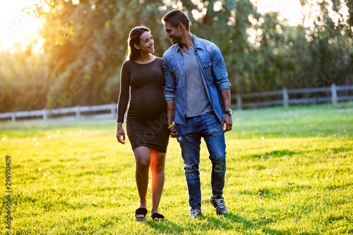 Beautiful pregnant couple relaxing with a walk in the park at sunset.