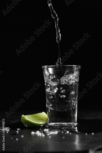 Obraz na plátně Pouring vodka into the shot glass on a black background with a blank space for a
