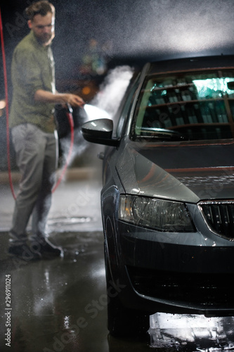 Young man washing his car in car wash. Cleaning Car Using High Pressure Water. Washing with soap. © Oleg Samoylov