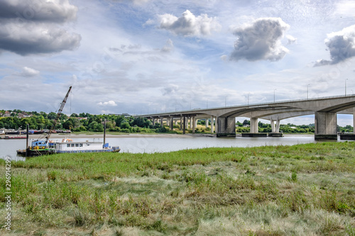  Distant view of a major motorway crossing, spanning the river medway, The foreground shows a moored up vessel by the marshes banks of the river.