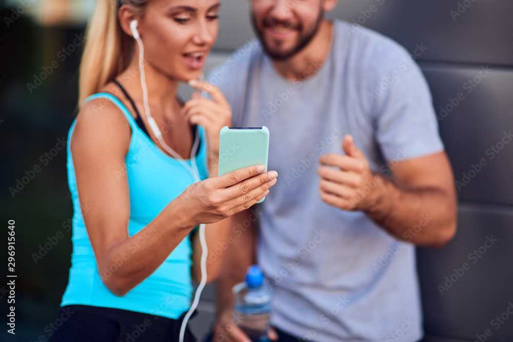 Modern woman and man jogging / exercising in urban surroundings and using cellphone at a pause / break.